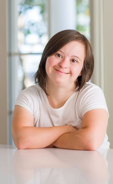 Down syndrome woman at home happy face smiling with crossed arms looking at the camera. Positive person.
